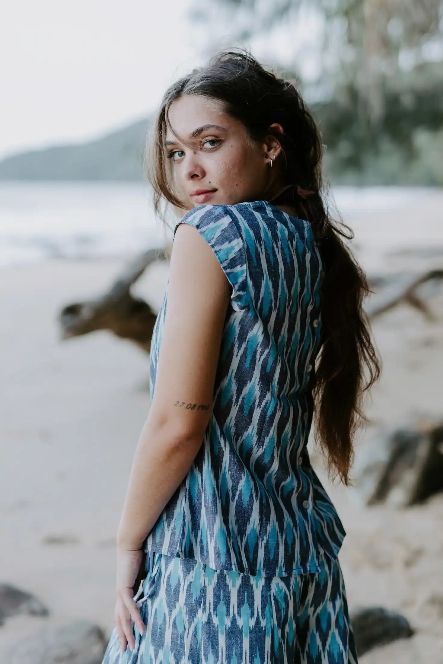 Handmade Firozi Ikat top in shades of blue, worn by a woman on a beach, showcasing ethical fashion crafted from lightweight cotton fabric